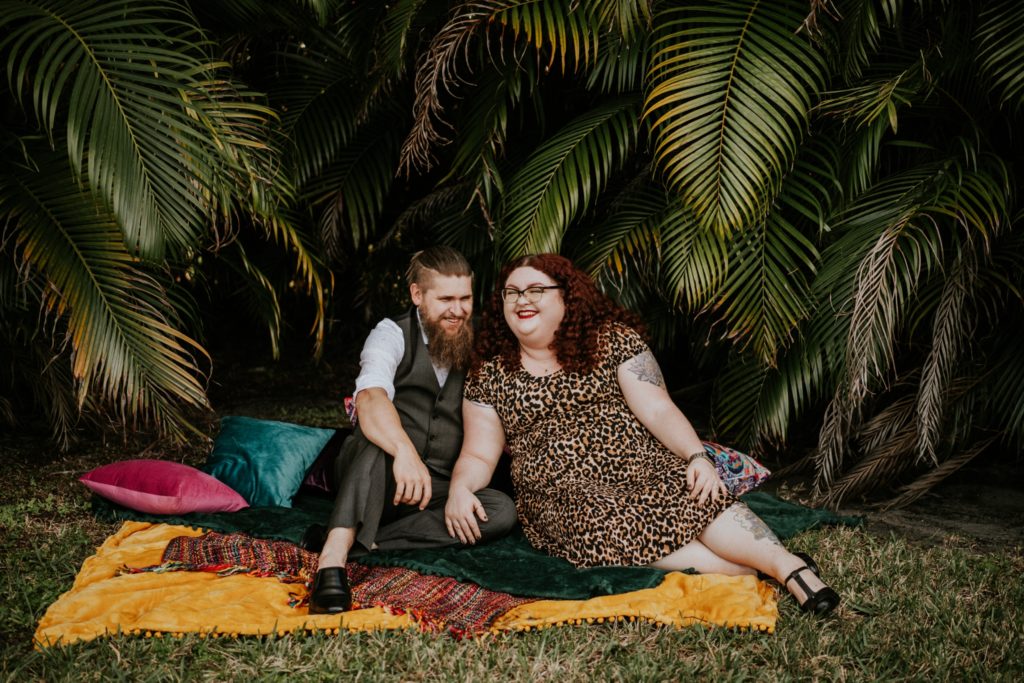 Matt & Nikki sit and laugh on jewel tone boho blanket and pillows for Palm Beach engagement