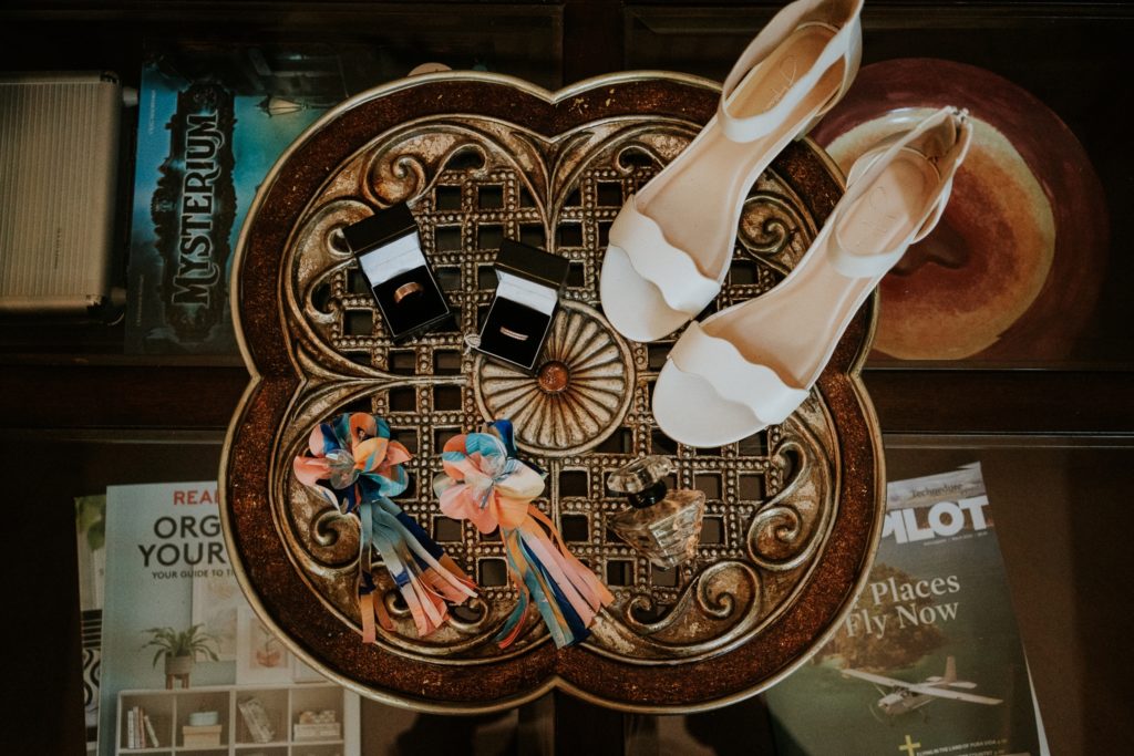 Wedding details shoes, colorful earrings, wedding rings, perfume bottle on glass coffee table