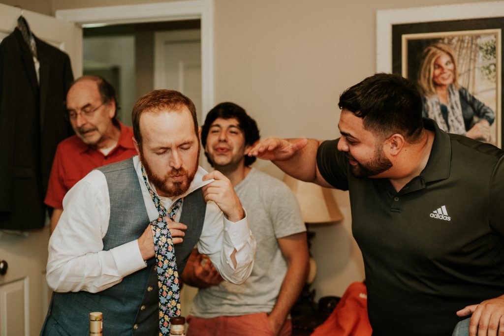 Groomsmen blow air down groom's shirt getting ready at-home wedding 