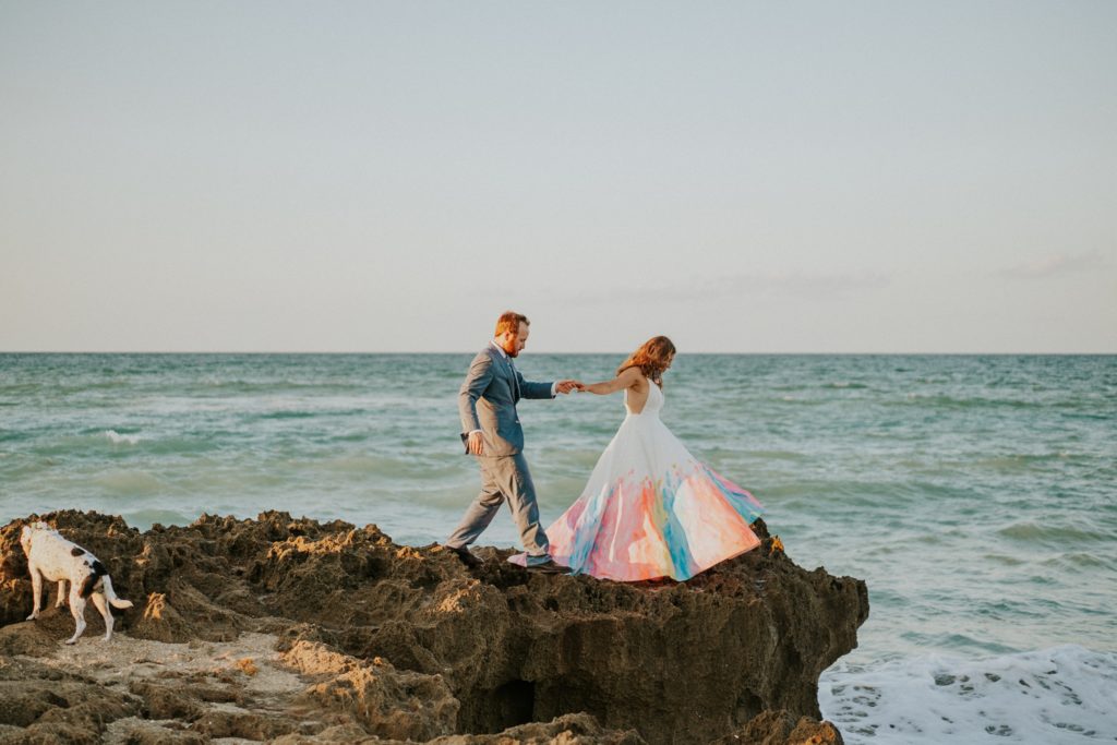 Bride leads groom walking on rocky beach House of Refuge Stuart FL elopement