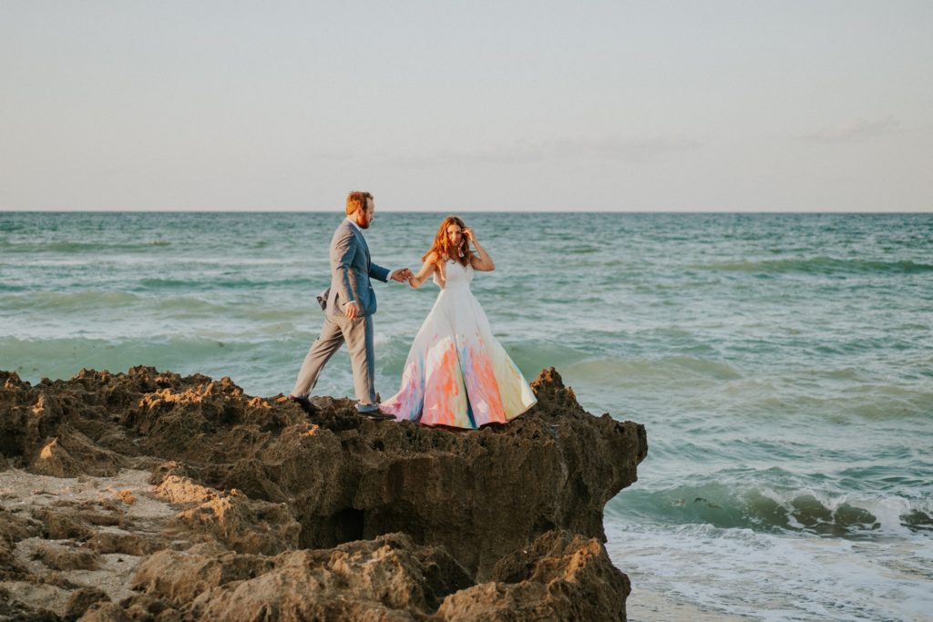 Bride leads groom walking on rocky beach House of Refuge Stuart Florida elopement