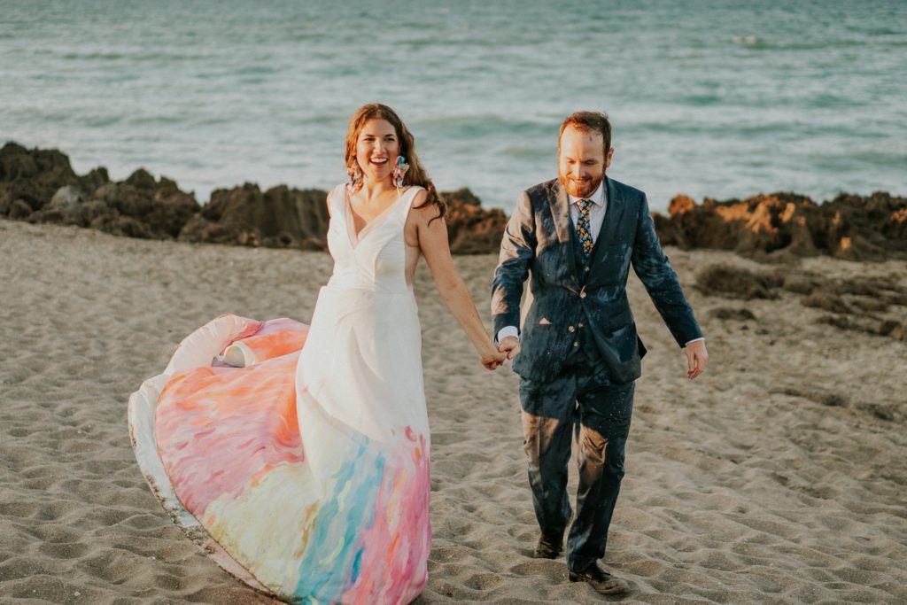 Bride and groom swing dress holding hands rocky beach Stuart FL elopement photography
