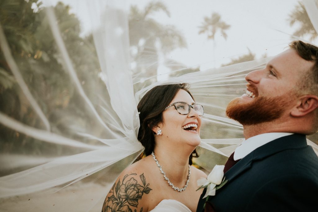 Bride with glasses and groom laugh under wedding veil