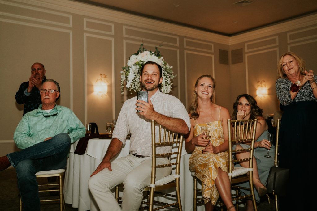 Wedding guests laugh and film reception toasts