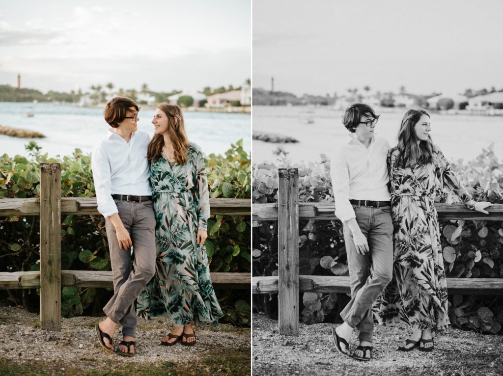 Bri and Aaron hold each other leaning on wooden fence with Jupiter lighthouse behind them