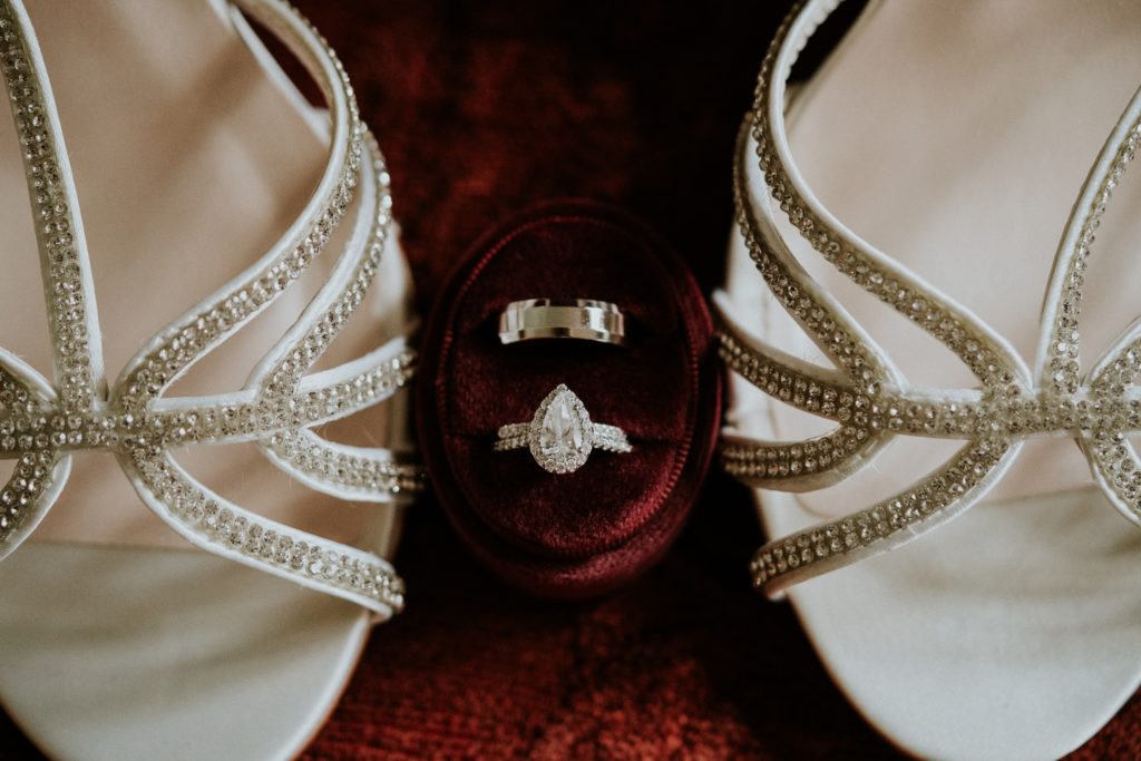 Casa Lantana wedding rings in burgundy ring box between white crystal heels