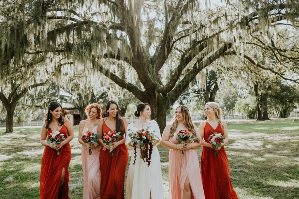 Casa Lantana wedding bride walks with bridesmaids in rust orange and blush pink dresses under spanish moss tree