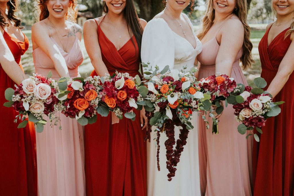 Bride and bridesmaids bouquet with burgundy red, orange, and pink roses and white calla lillies