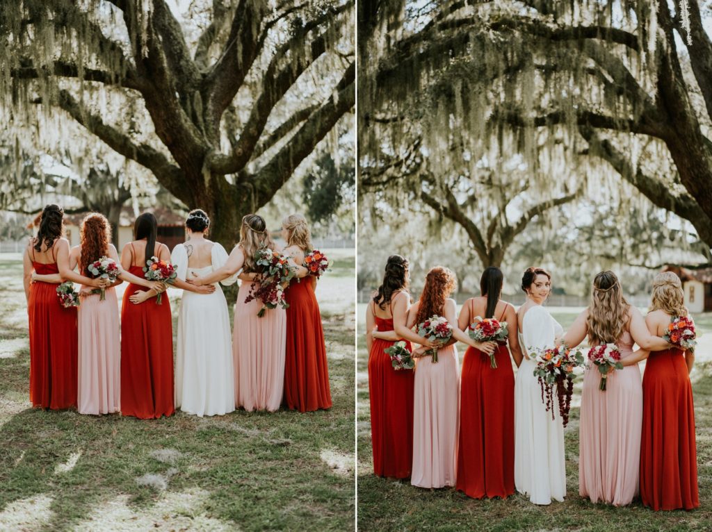 View of the back of bridesmaids in rust orange and blush pink dresses with bride turning around under spanish moss tree at Casa Lantana Brandon FL wedding