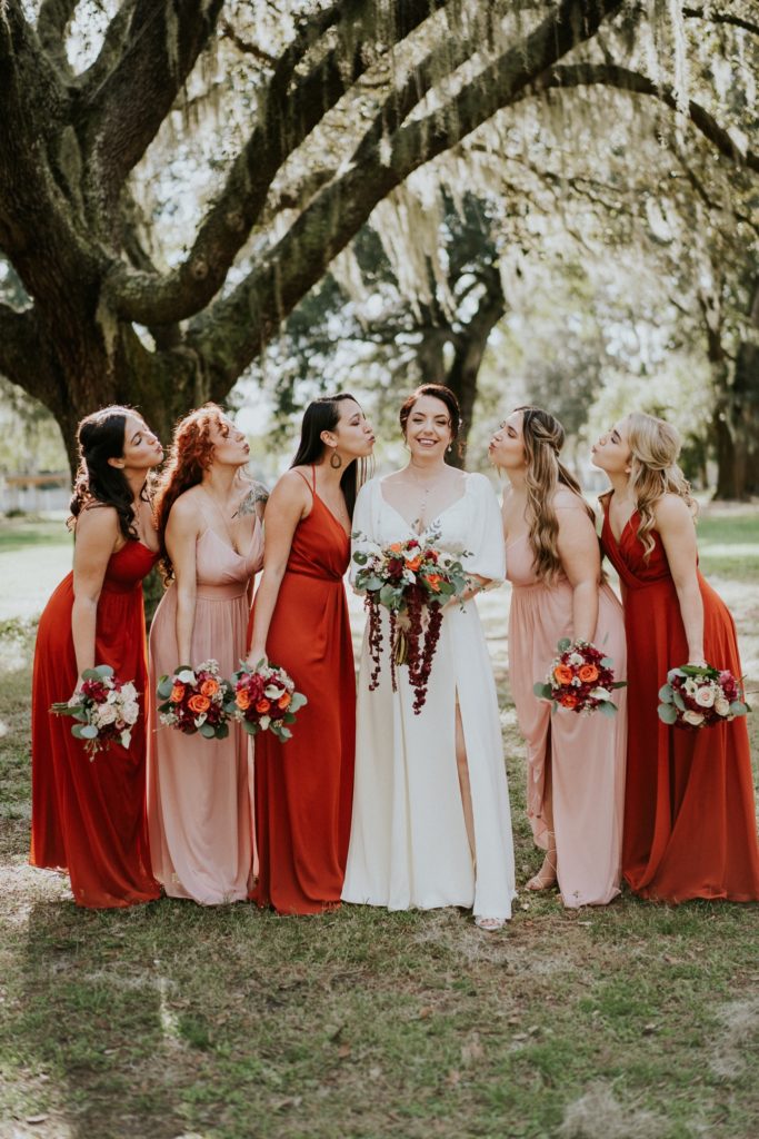 Casa Lantana wedding bridesmaids in orange and pink dresses kiss bride under spanish moss tree