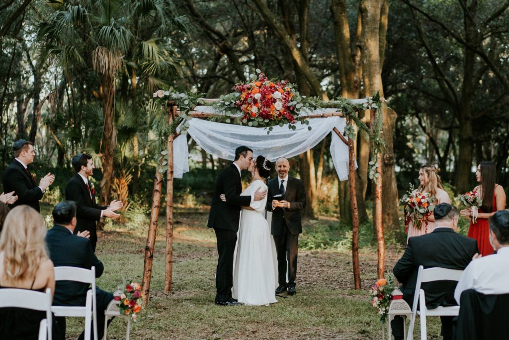 Bride and groom first kiss under chuppah at Casa Lantana wedding in Brandon FL