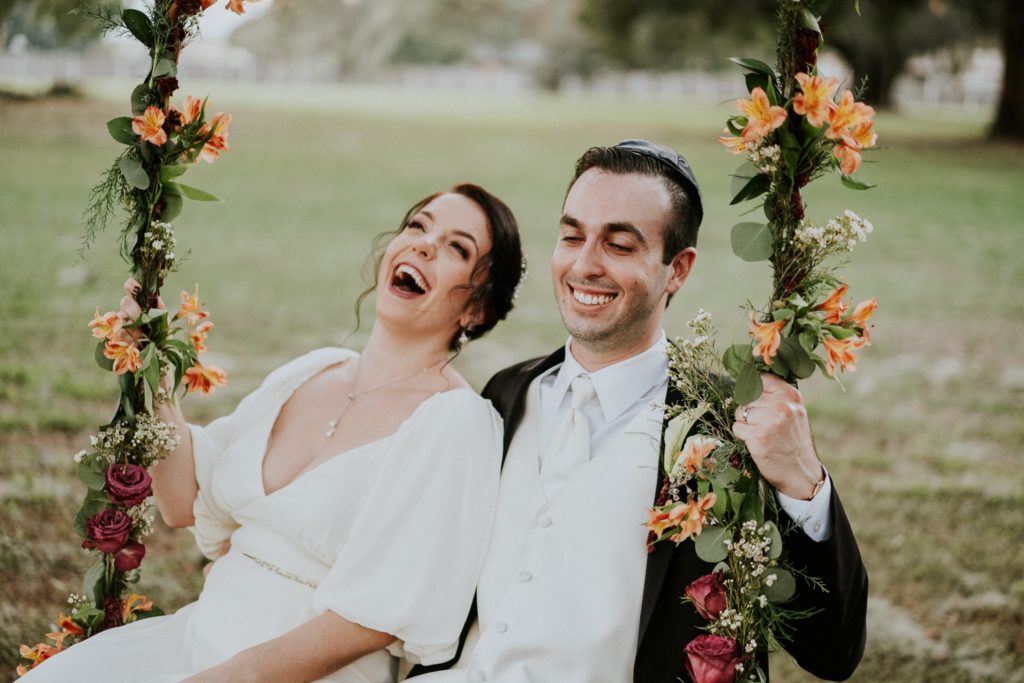 Bride and groom laughing on floral wedding swing