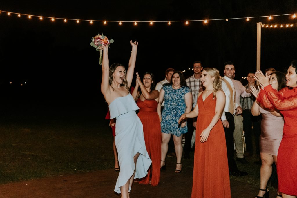 Wedding guests cheers and holds up bouquet toss catch