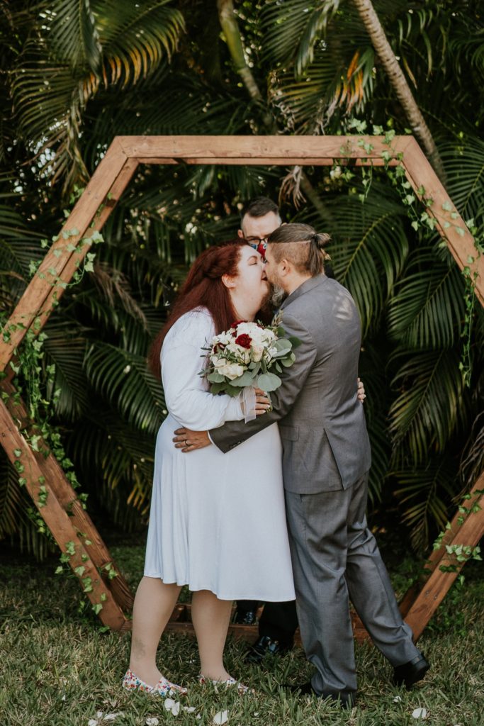 Bride and groom kiss under geometric hexagon arch in backyard wedding ceremony
