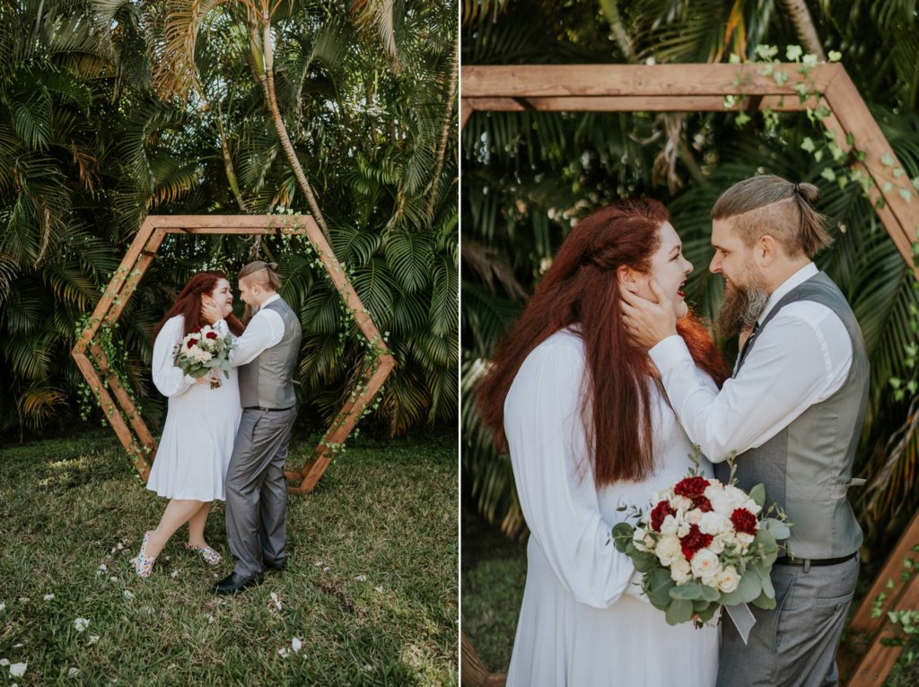 Groom holds face of redhead bride under geometric hexagon arch in West Palm Beach FL backyard wedding
