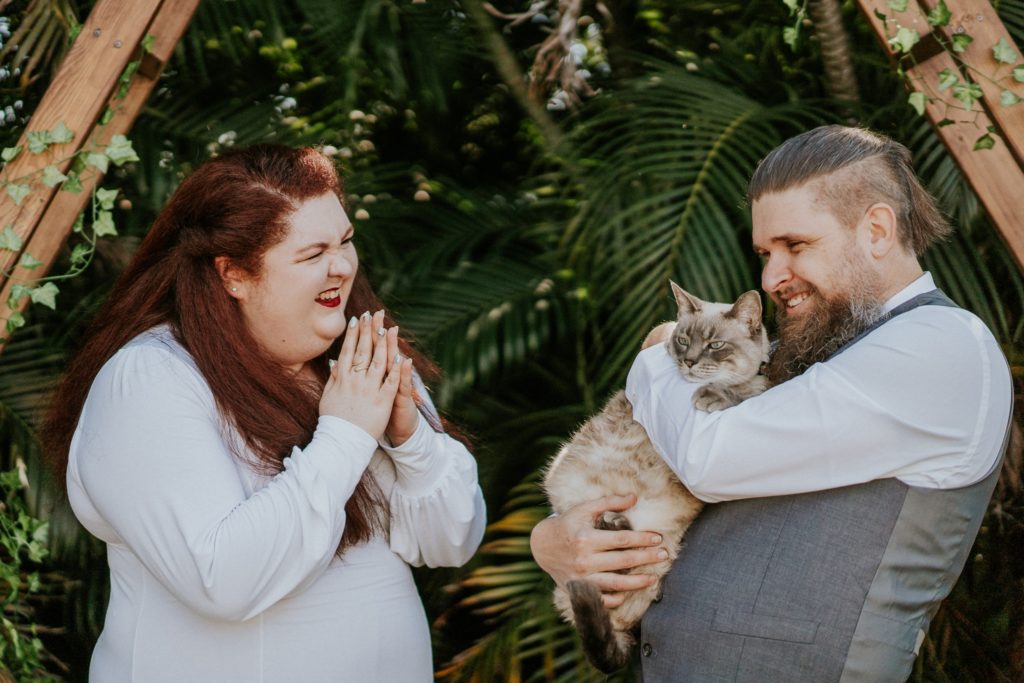 Redhead bride laughs at groom holding their cat in West Palm Beach FL backyard wedding