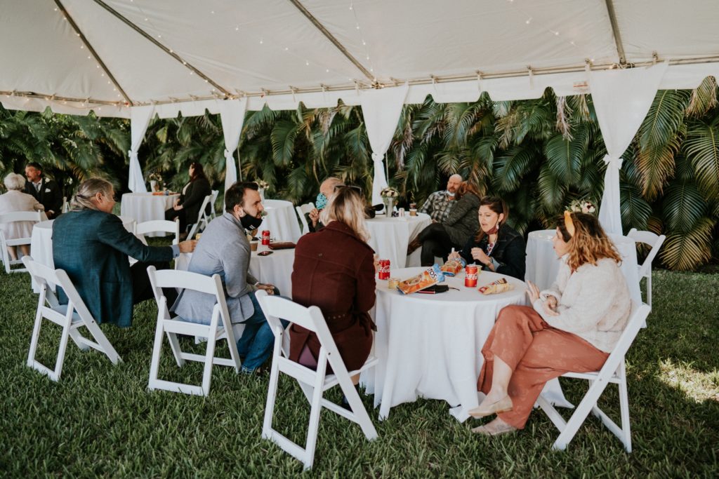 Guests eat under reception tent in West Palm Beach Florida backyard wedding