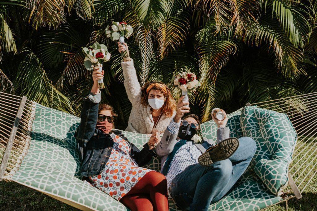 Bridesmaids and guest lift bouquets while laying on hammock in West Palm Beach FL backyard wedding