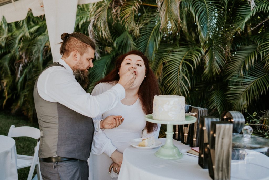 Groom feeds bride in backyard wedding cake cutting