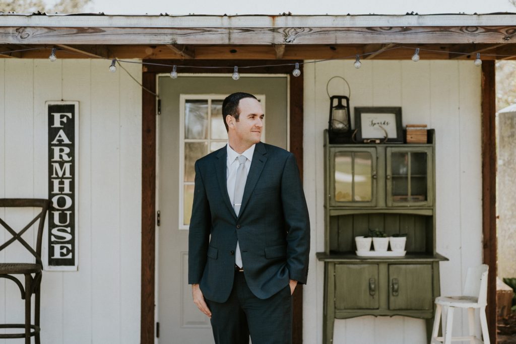 Groom looks away from camera in front of farmhouse