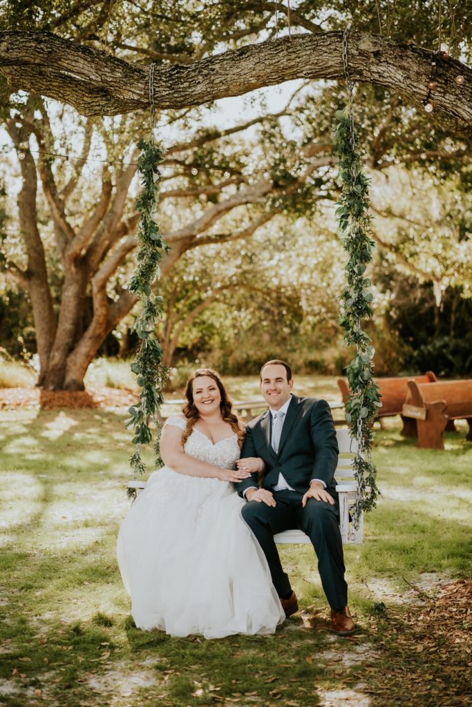 Bride and groom sit on swing wrapped in greenery at Cattleya Chapel rustic wedding Florida