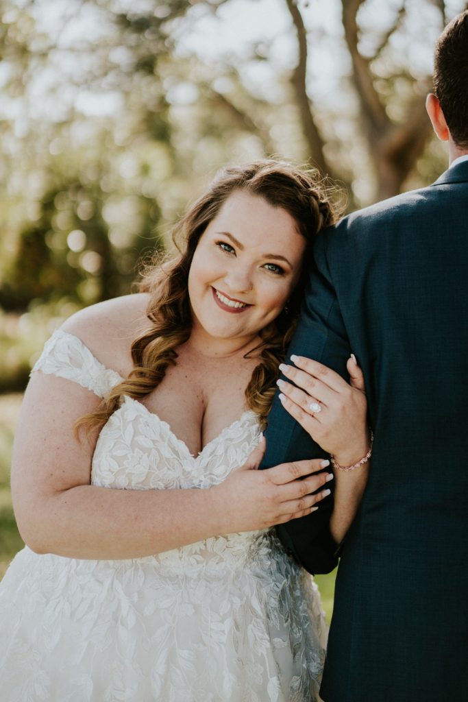 Bride smiles at camera while holding groom's arm