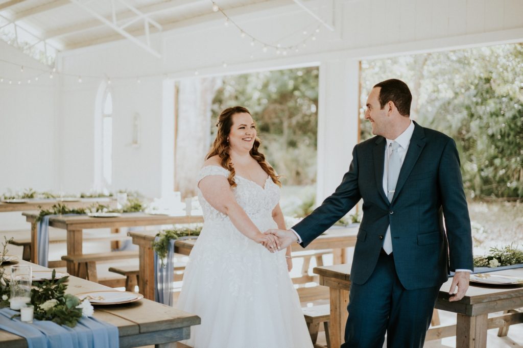 Groom leads bride through white FL wedding barn venue