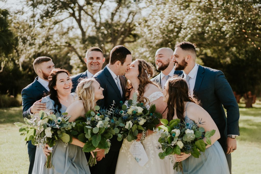 Wedding party group looks at couple as they kiss