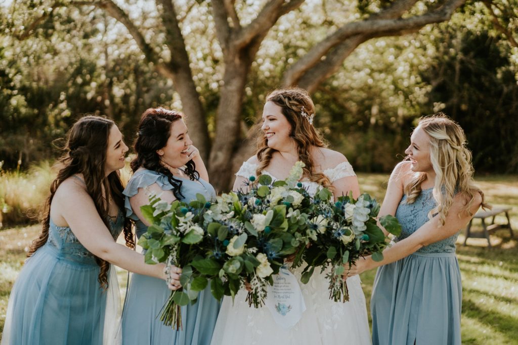 Bridesmaids in dusty blue Azazie dresses hold bouquets together at Cattleya Chapel