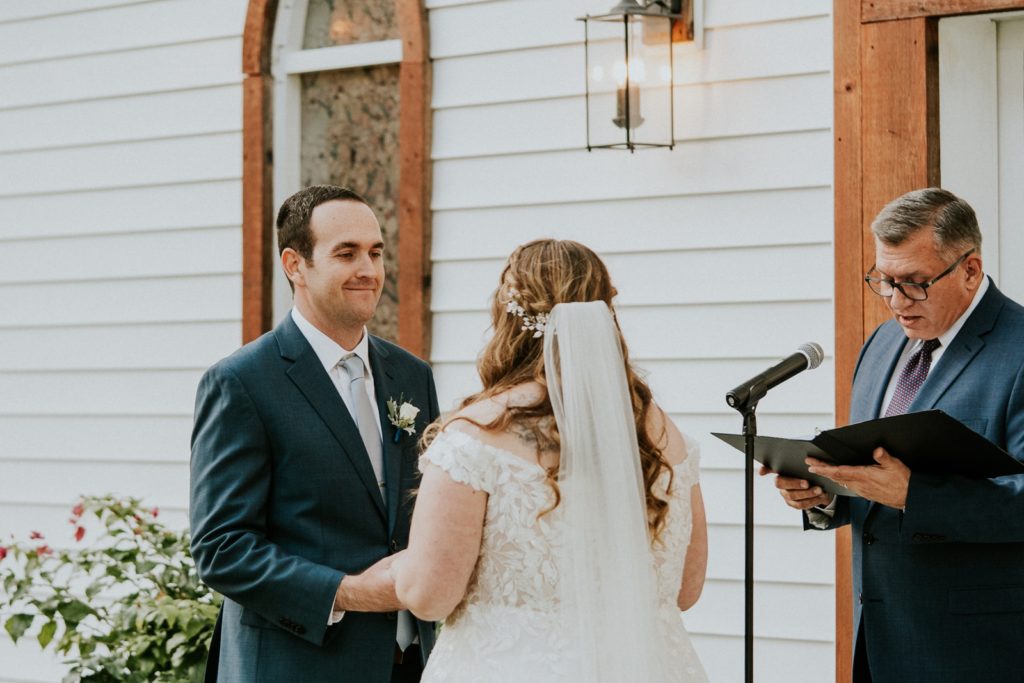 Groom smiles at bride during outdoor ceremony