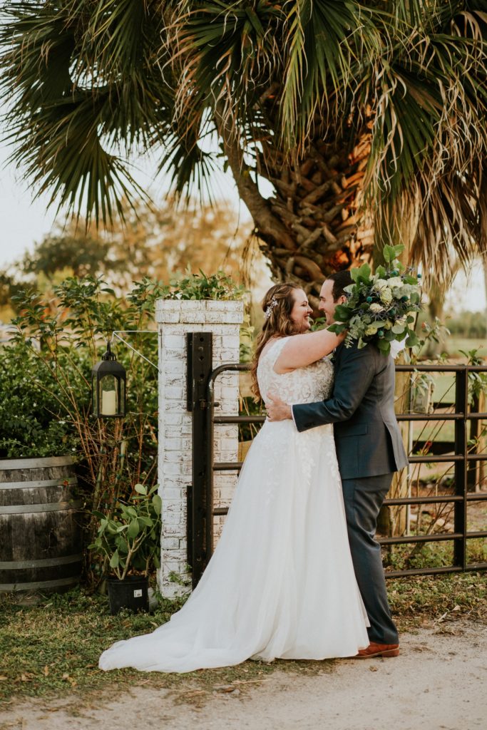Couple hugs by rustic farm fence under palm tree at Cattleya Chapel FL wedding