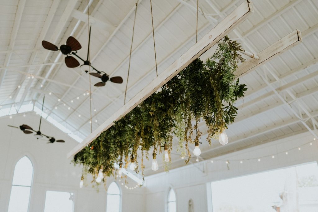 Hanging greenery chandelier with lightbulbs in white FL wedding barn