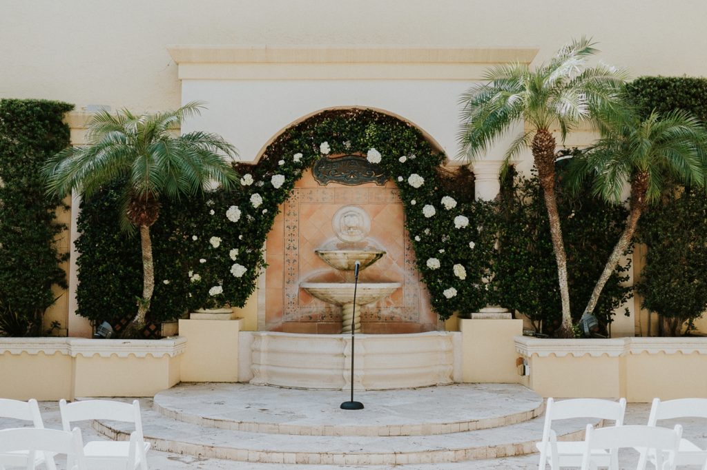 Courtyard wedding ceremony stone fountain surrounded by greenery wall with white roses