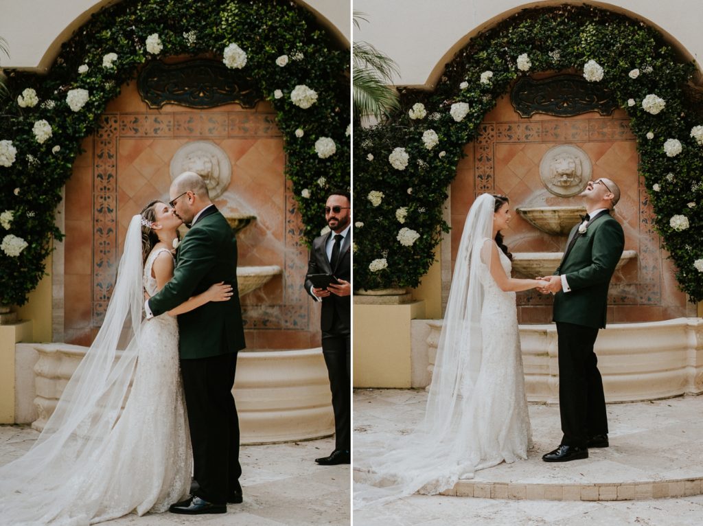 Benvenuto wedding ceremony first kiss in front of fountain with white rose greenery wall