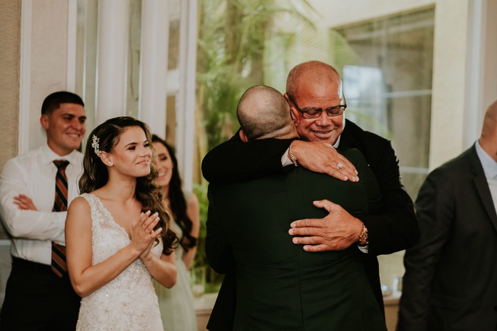 Bride's father hugs groom as bride smiles