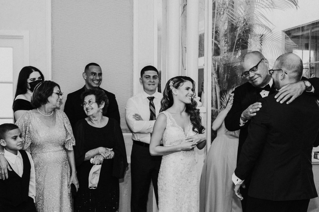 Black and white photo of bride's family smiling and hugging groom