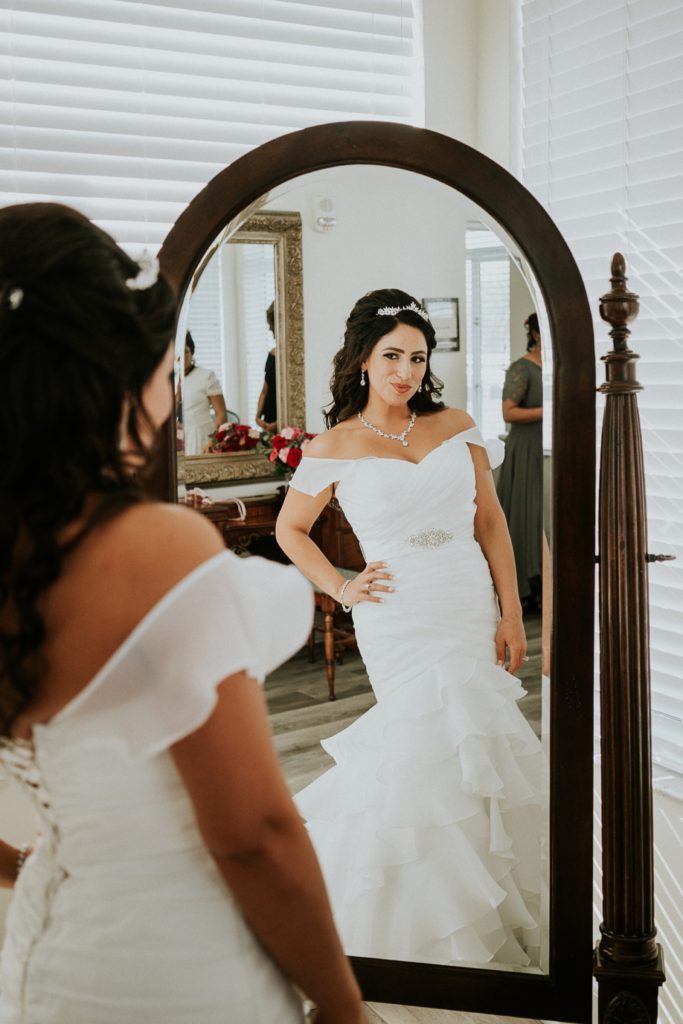 Bride wearing wedding dress looks at herself in mirror in Tuckahoe Mansion bridal suite