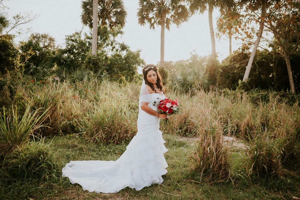 Jensen Beach FL wedding photography bride holding pink rose bouquet in grassy field with palm trees at sunset