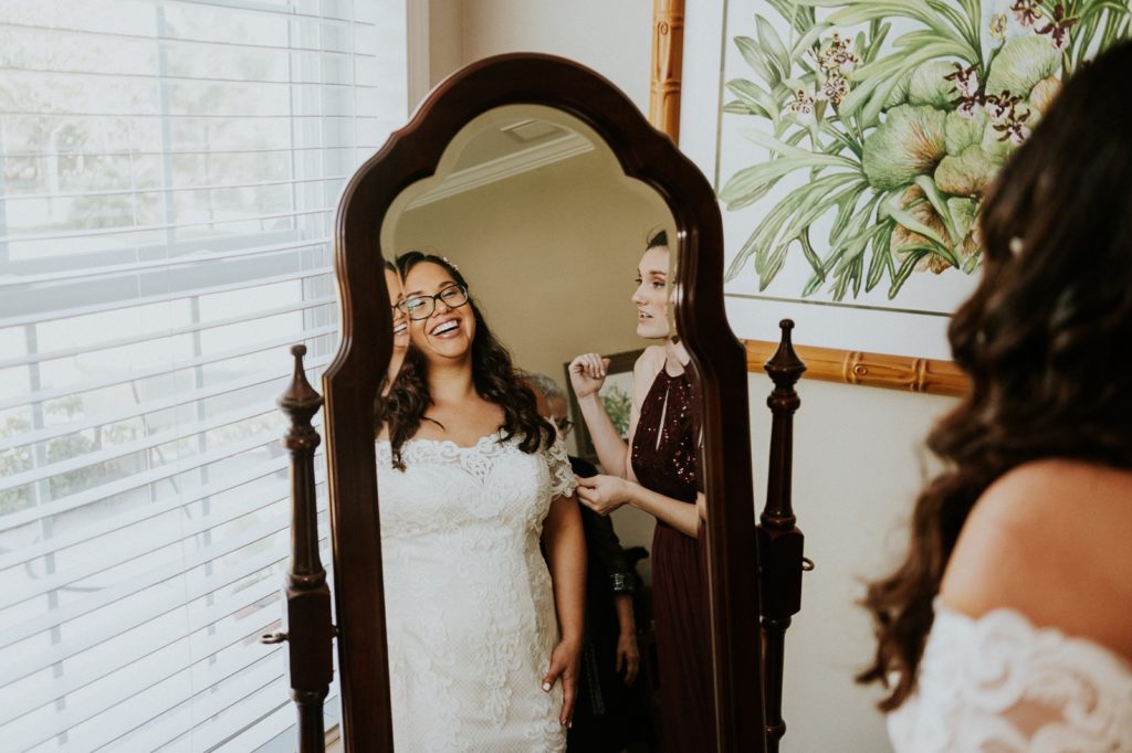 Bride wearing lace wedding dress laughs in mirror