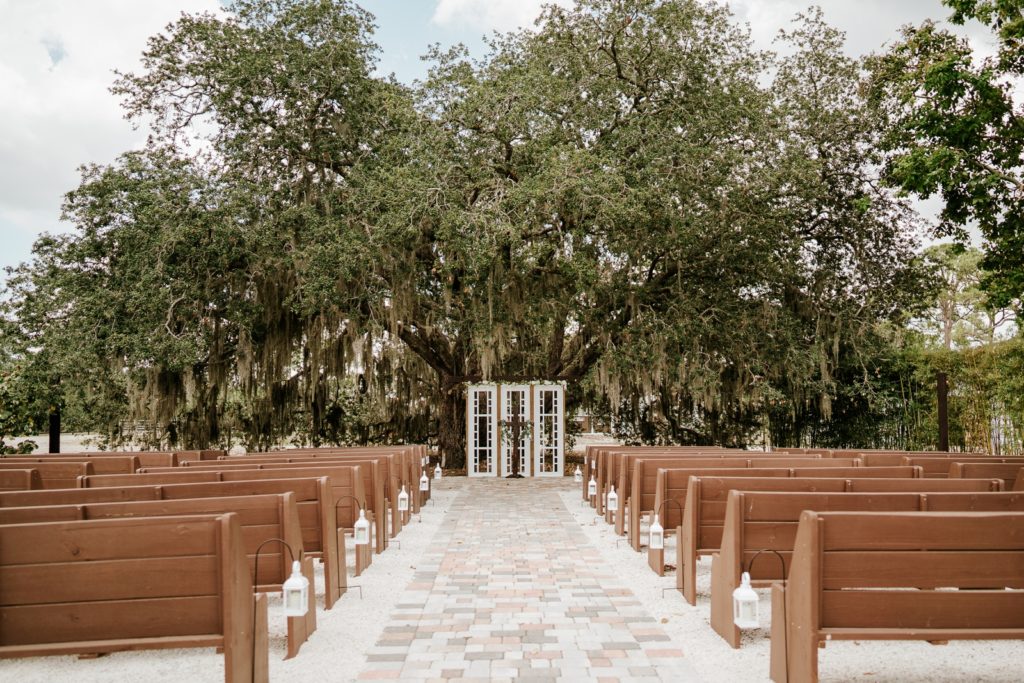Ever After Farms Ranch ceremony with wood benches and cross under spanish moss tree