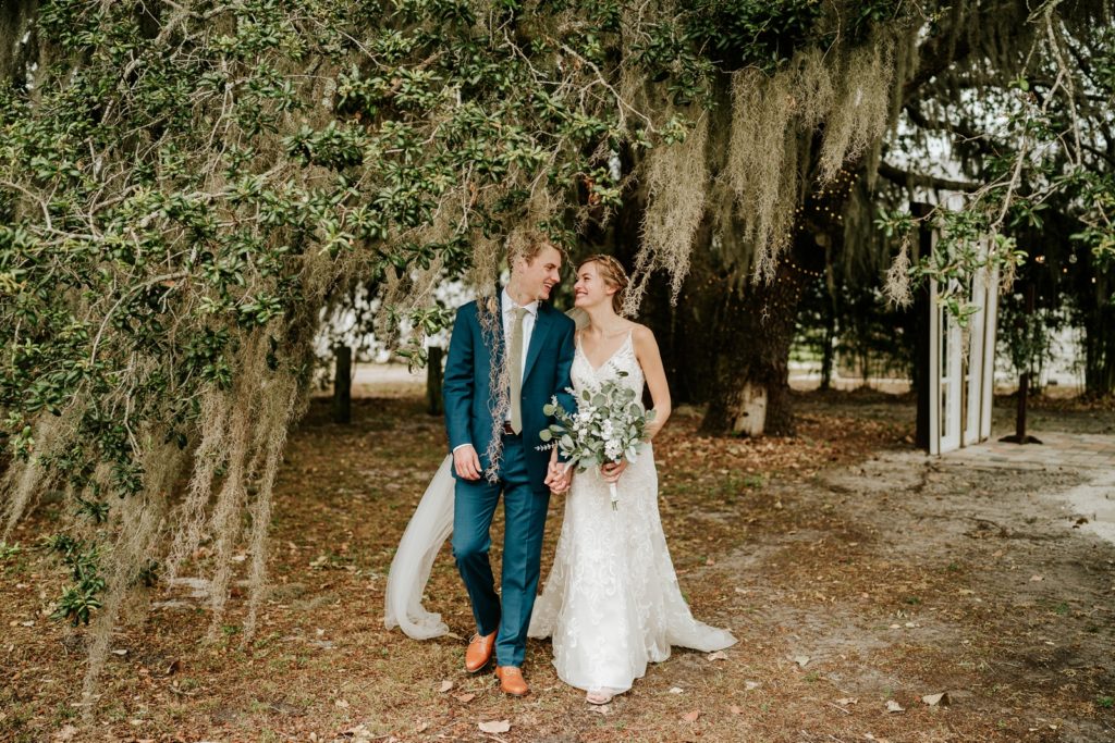 Bride and groom walk under spanish moss tree at Ever After Farms Ranch Wedding