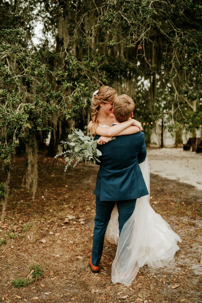 Groom picks up bride and spins her around under spanish moss tree
