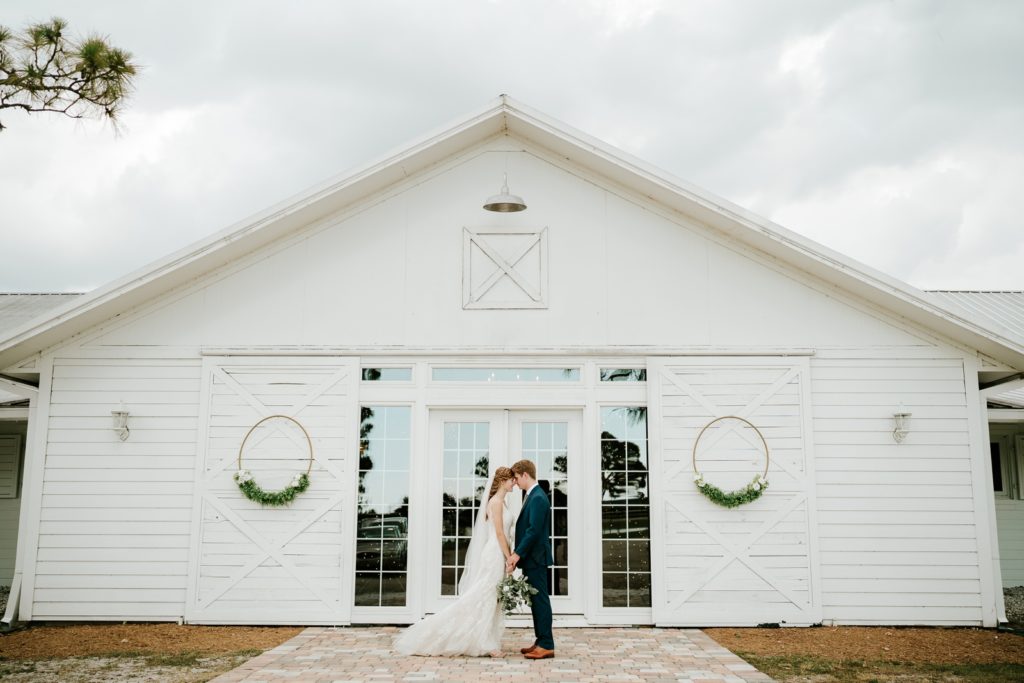 Bride and groom hold hands in front of Ever After Farms Ranch white wedding barn in Indiantown FL
