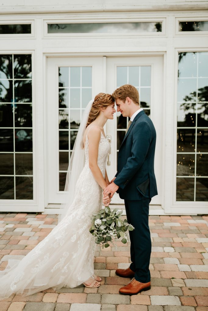 Bride and groom hold hands in front of Ever After Farms Ranch white wedding barn glass doors