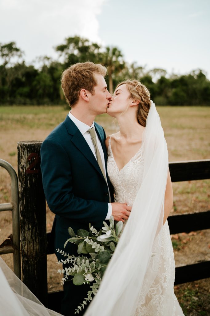 Bride and groom kiss by farm fence at Ever After Farms Ranch wedding