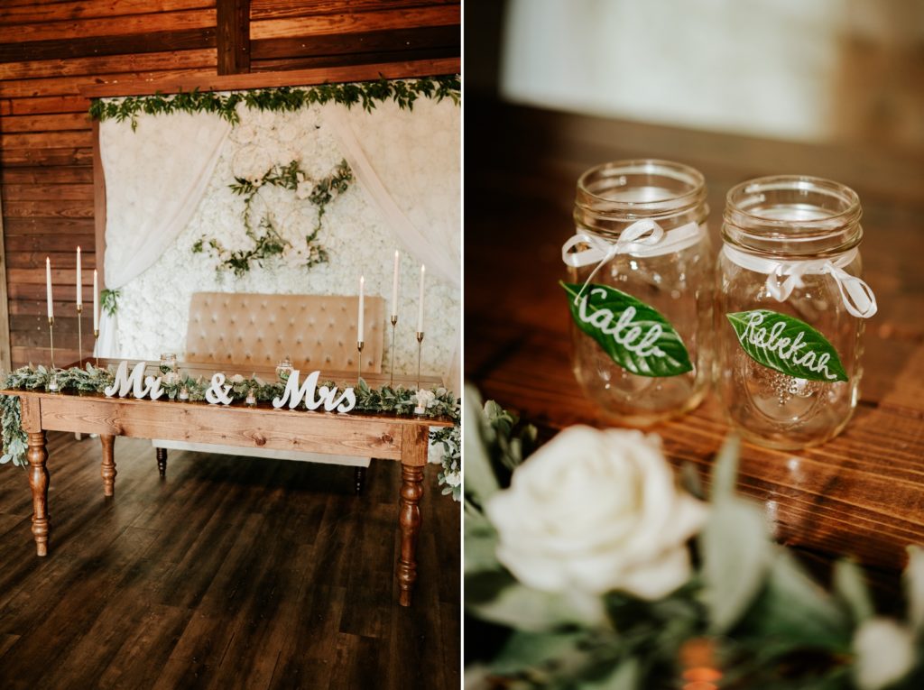 Rustic wood sweetheart table with white roses, greenery, and mason jar favors