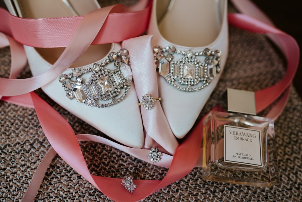 Wedding details bejeweled white shoes, rhinestone earrings, engagement ring, and Vera Wang Embrace perfume on pink ribbon