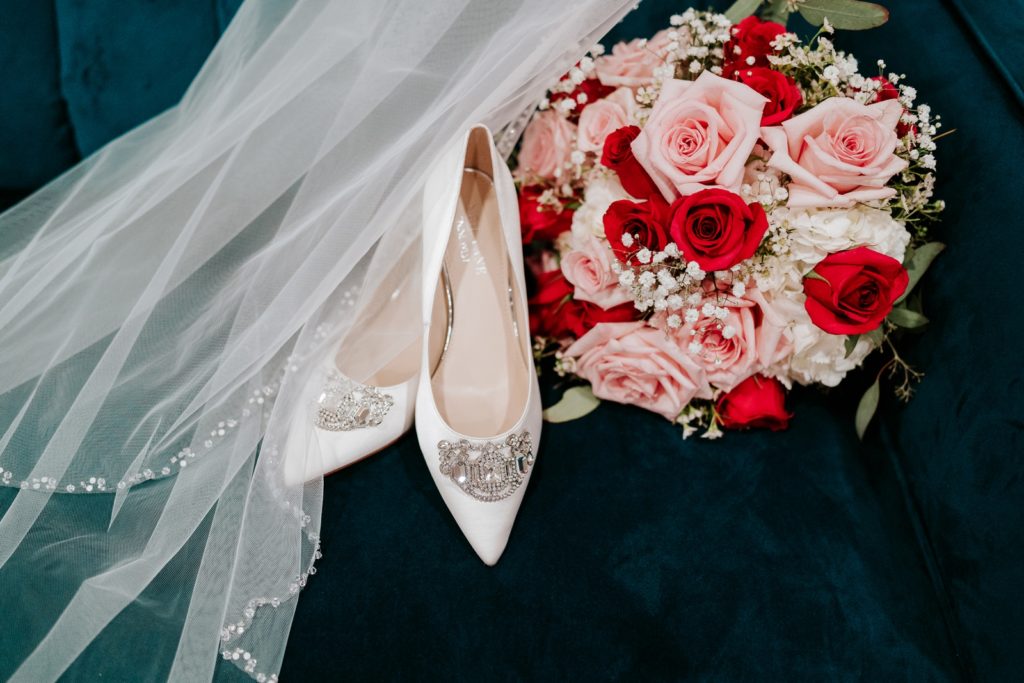 Wedding shoes, veil, and pink and red rose bouquet on blue velvet