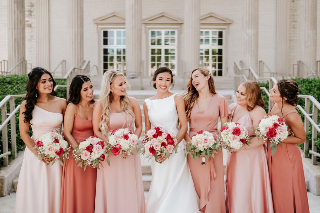 Bride with bridesmaids in pink dresses laugh outside Family Church Downtown West Palm Beach FL