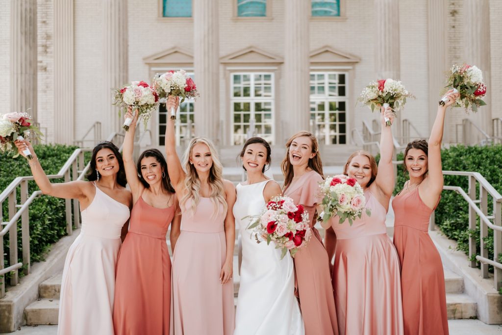 Bride and bridesmaids hold bouquets in the air outside of Family Church Downtown West Palm Beach FL